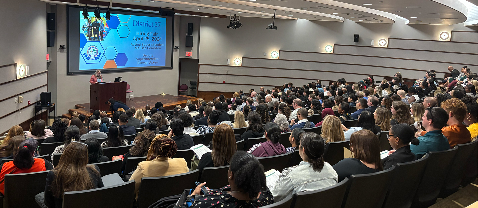 District 27 hiring fair presentation with attendees seated in an auditorium